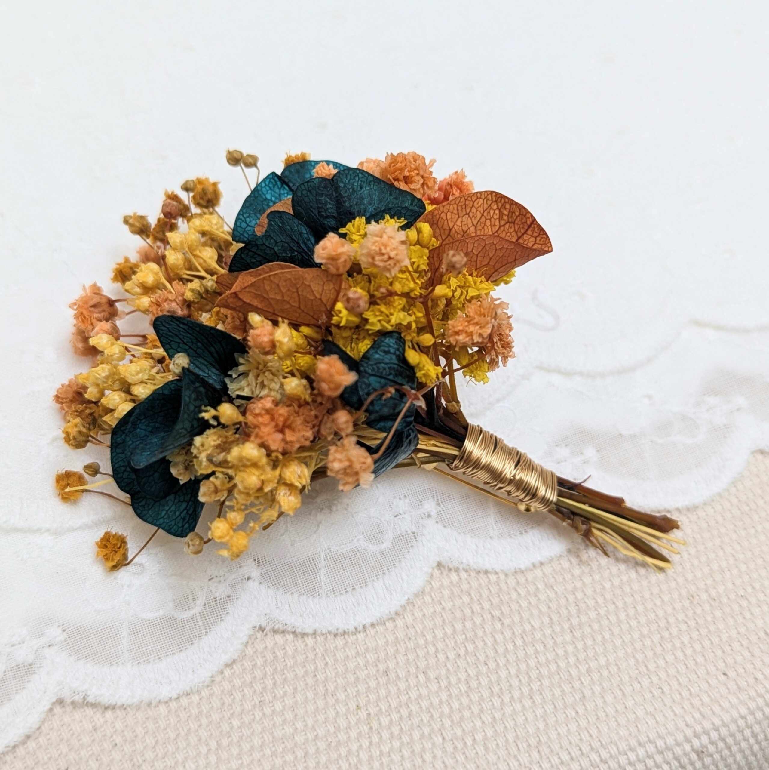 Boutonnière de marié artisanale en fleurs stabilisées oranges et bleues verts, Nila